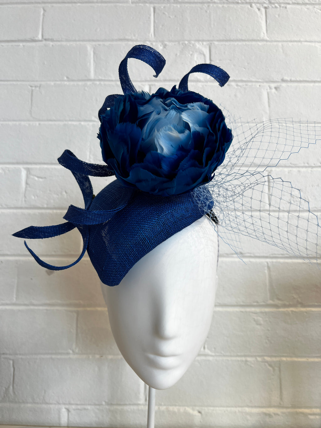 Navy blue flower headpiece on a white mannequin head against a textured white wall.