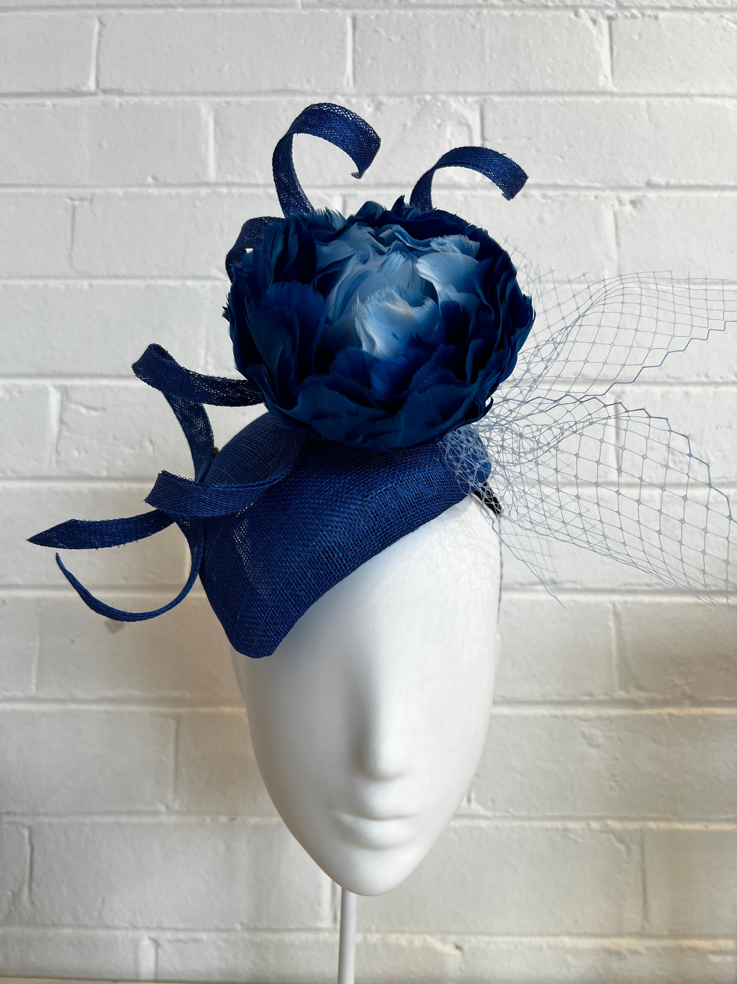 Navy blue flower headpiece on a white mannequin head against a textured white wall.